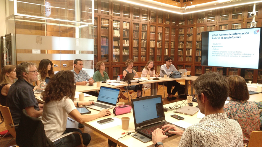 Fotografía de los asistentes a la sesión de trabajo en una sala de reuniones y con una pantalla de fondo.